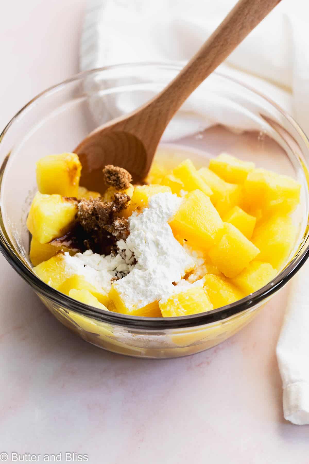 A mixing bowl full of pineapple chunks, brown sugar and cornstarch.