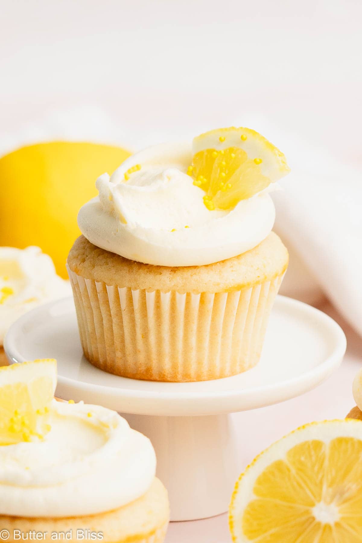 Pretty frosted lemon cupcake on a mini cupcake stand garnished with a lemon wedge.