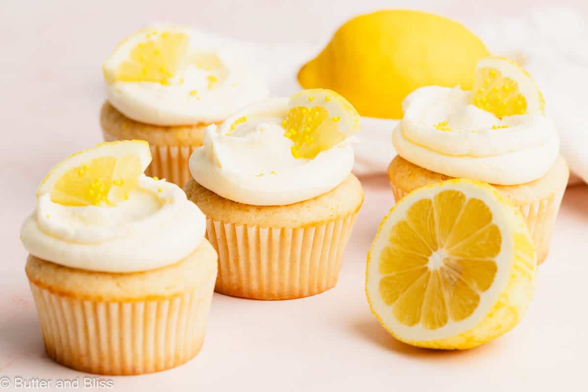 A pretty small batch of lemon cupcakes frosted and decorated with lemon wedges on a table.