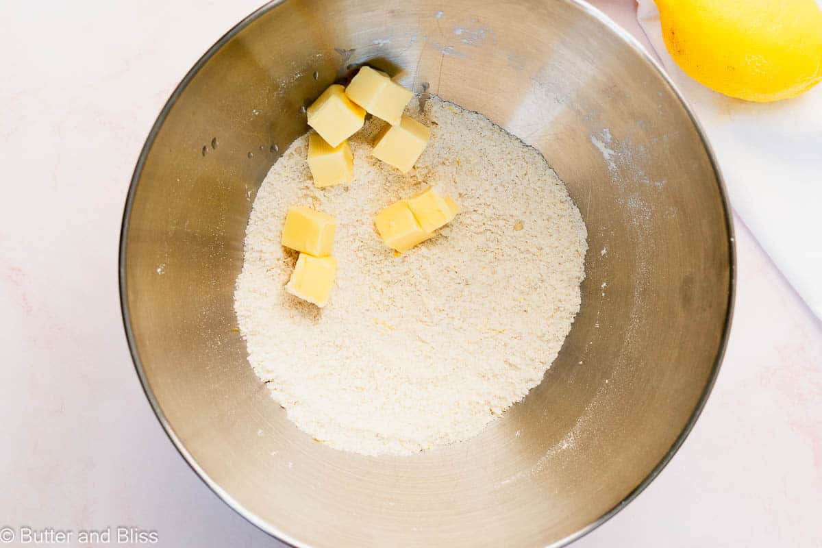 Butter cubes added to the dry ingredients in a mixing bowl.