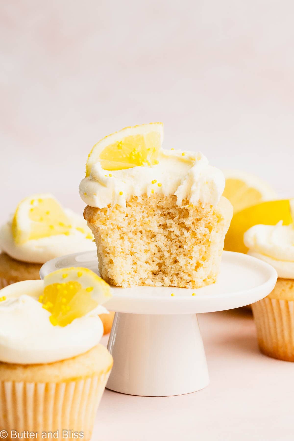 Small batch lemon cupcakes on a table frosted with lemon buttercream with a bite out of one cupcake.