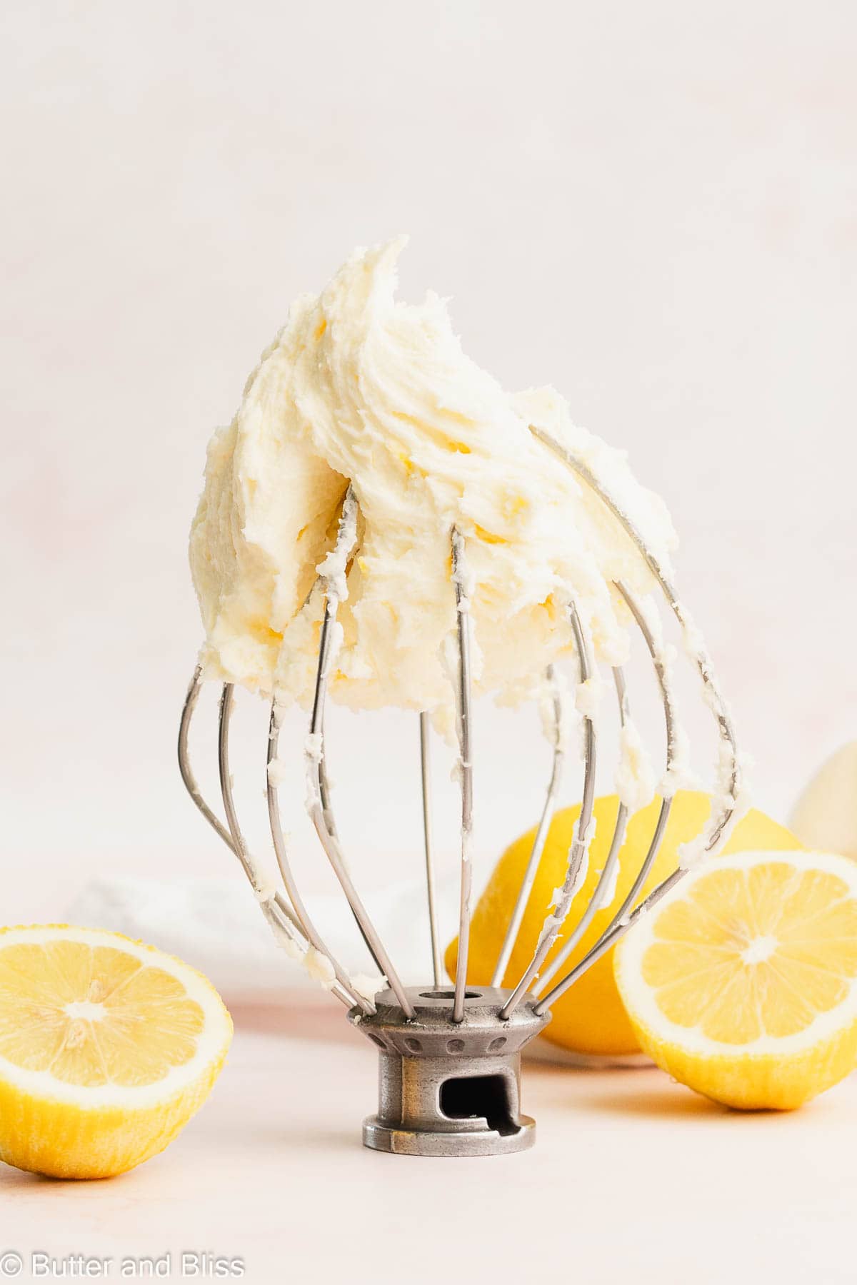 Fluffy lemon buttercream frosting on a mixer whisk arranged on a table with lemons.