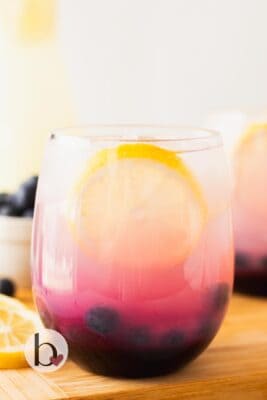 A glass of blueberry lemonade with lemon slice and fresh blueberries.