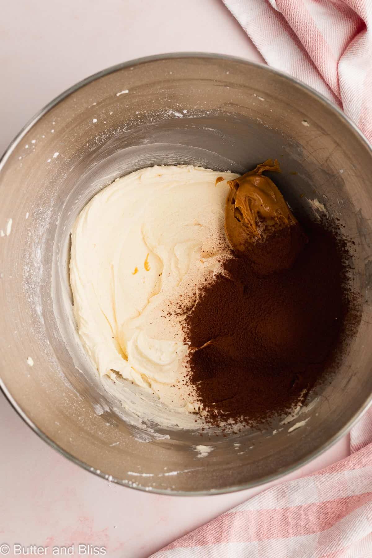 Cocoa and peanut butter being added to vanilla frosting in a mixing bowl.