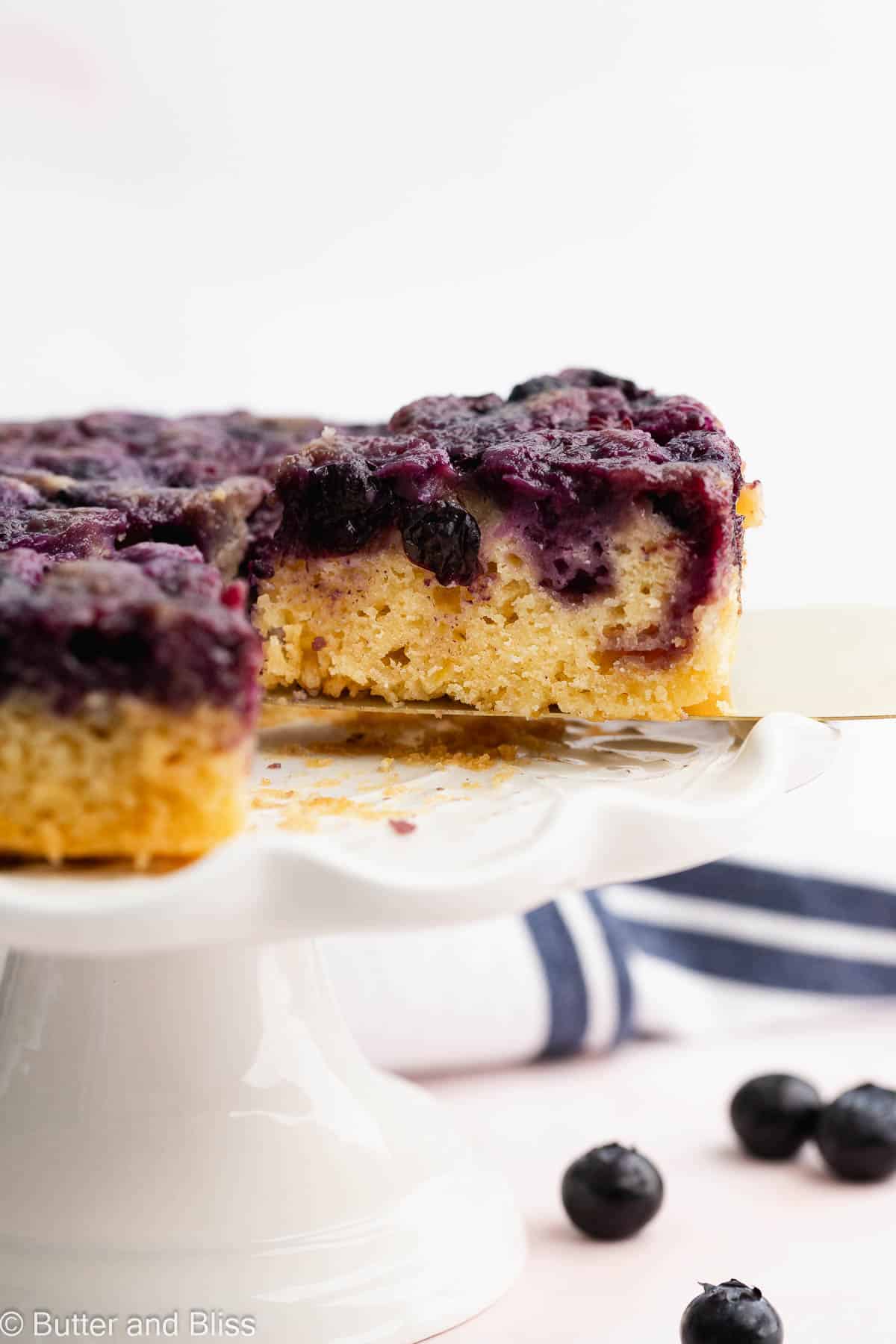 A slice of blueberry lemon upside down cake being cut from the small cake.