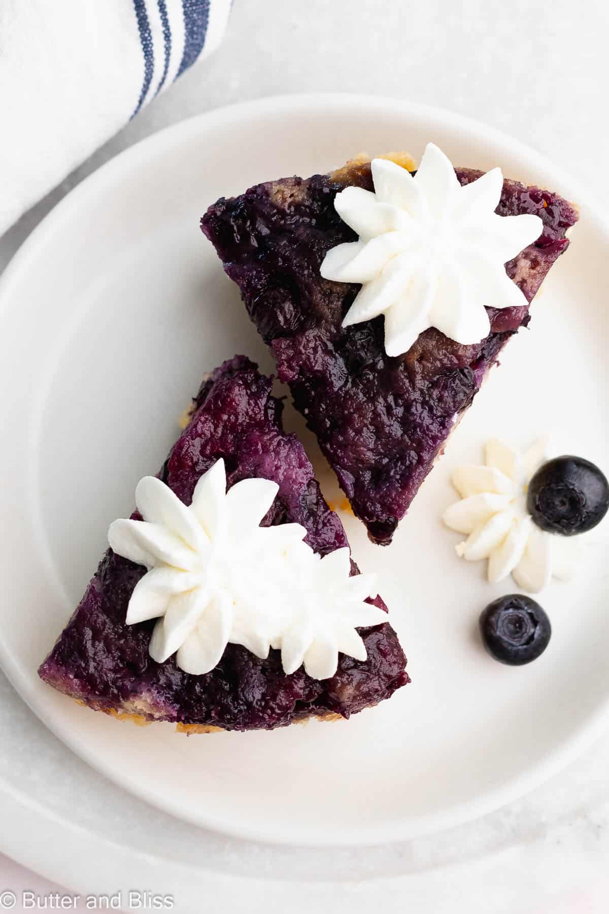 Jammy blueberries an whipped cream stars on top of two small slices of upside down cake.