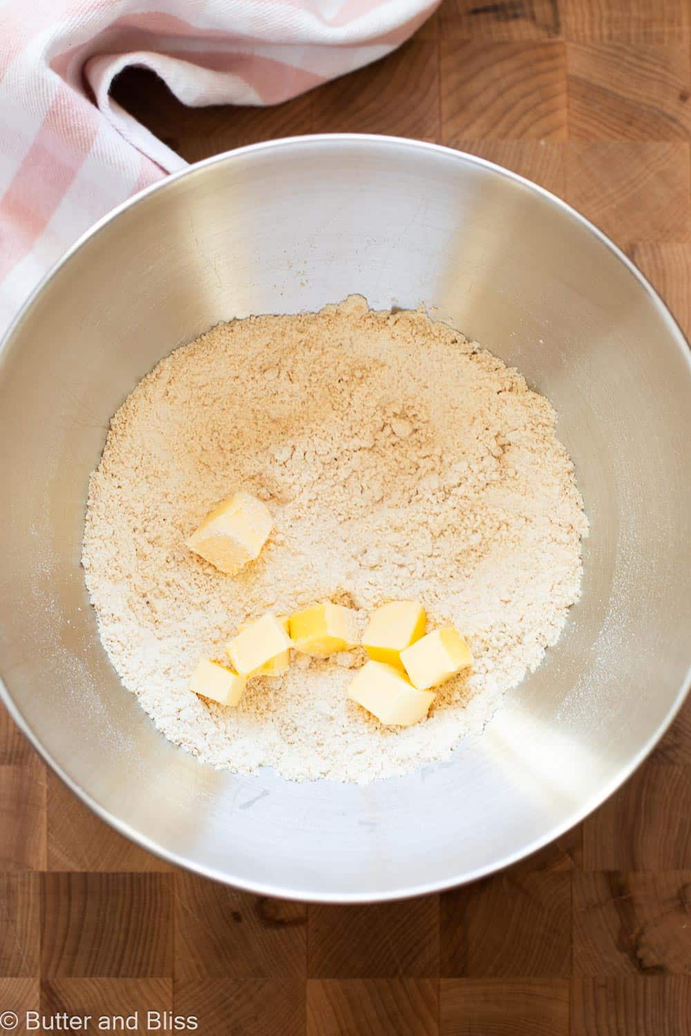 Butter cubes added to dry ingredients in a mixing bowl.