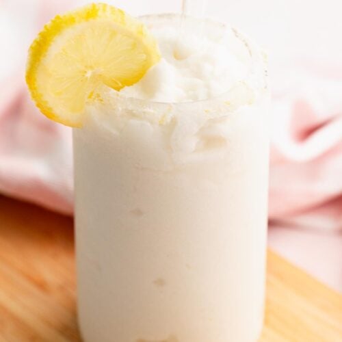 Creamy whipped frozen lemonade in a pretty glass with a sugar rim and lemon slice.