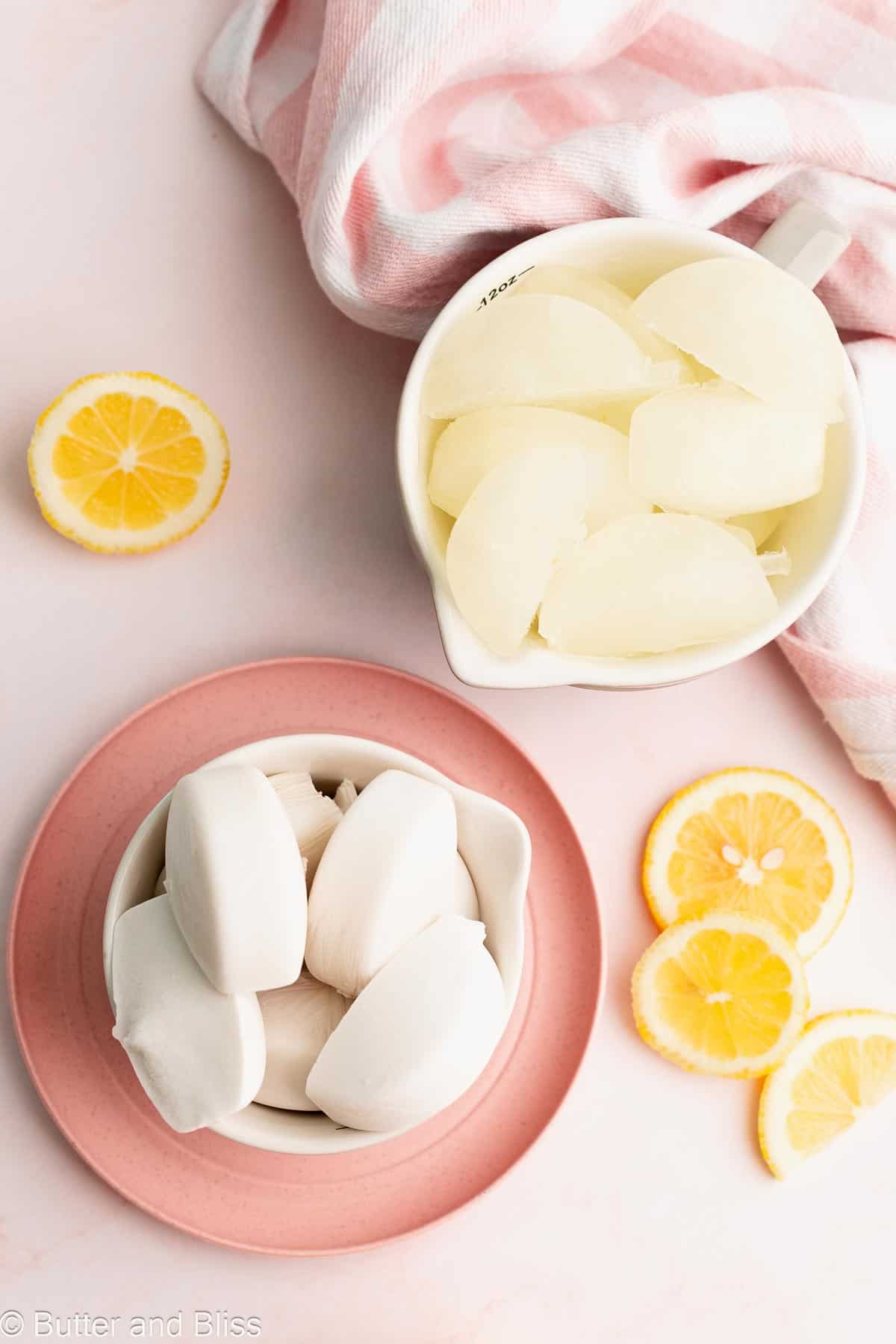 Lemonade and coconut milk ice cubes in small bowls on a table.