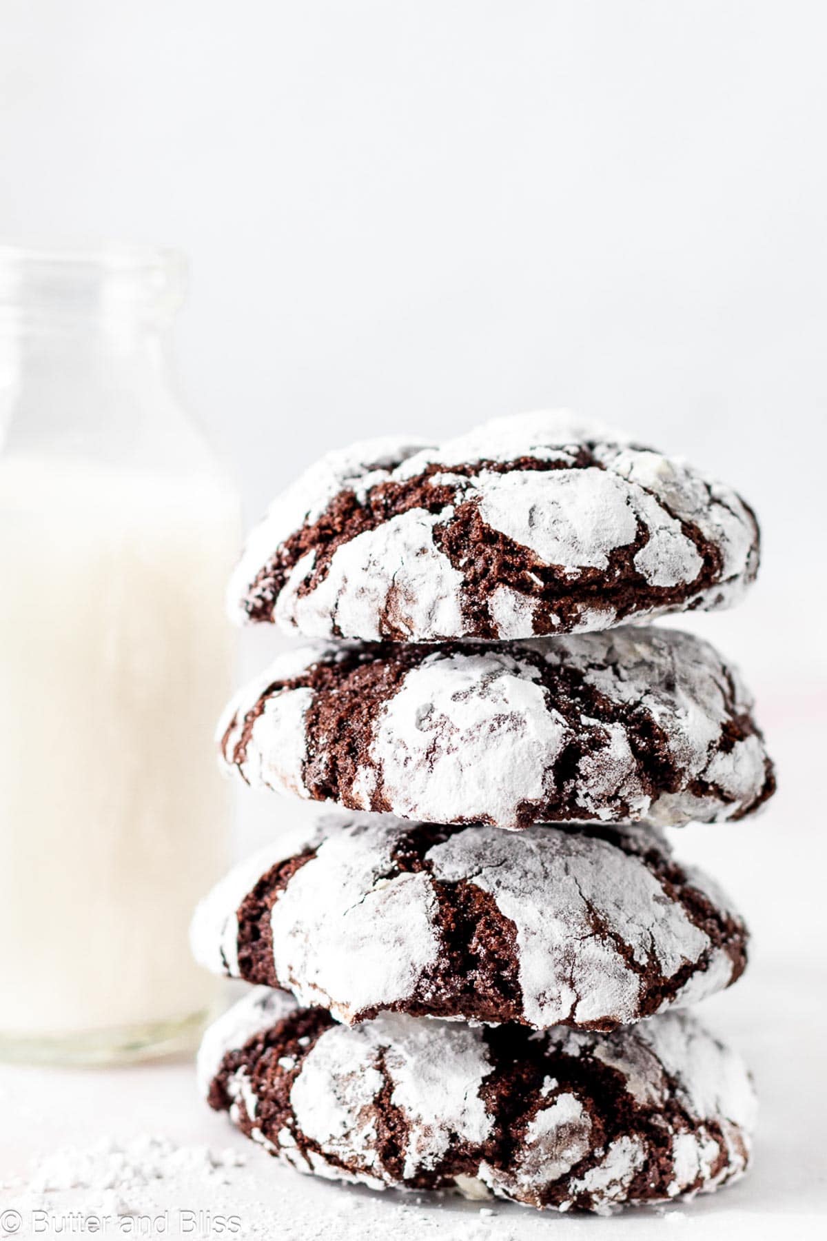 A stack of chocolate and powdered sugar cookies next to a glass of milk.