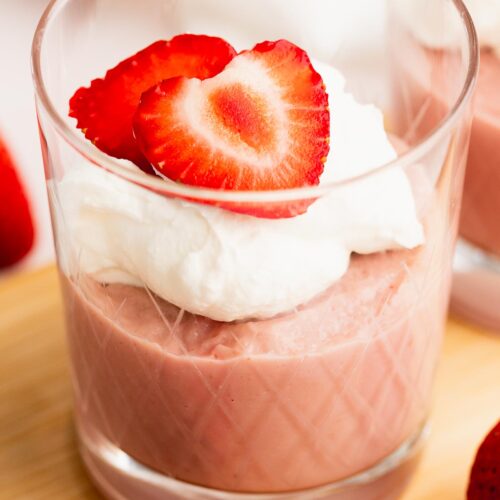 Single serving of strawberry pudding topped with whipped cream and strawberry slices in a glass.