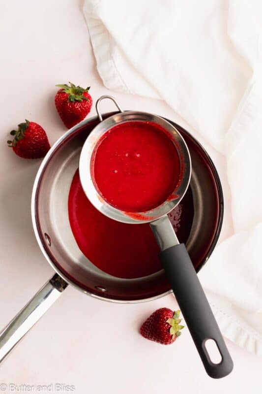 Strawberry puree poured through a mesh strainer into a saucepan.