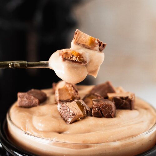 Creamy milky way pudding on a small spoon with pieces of candy on top.