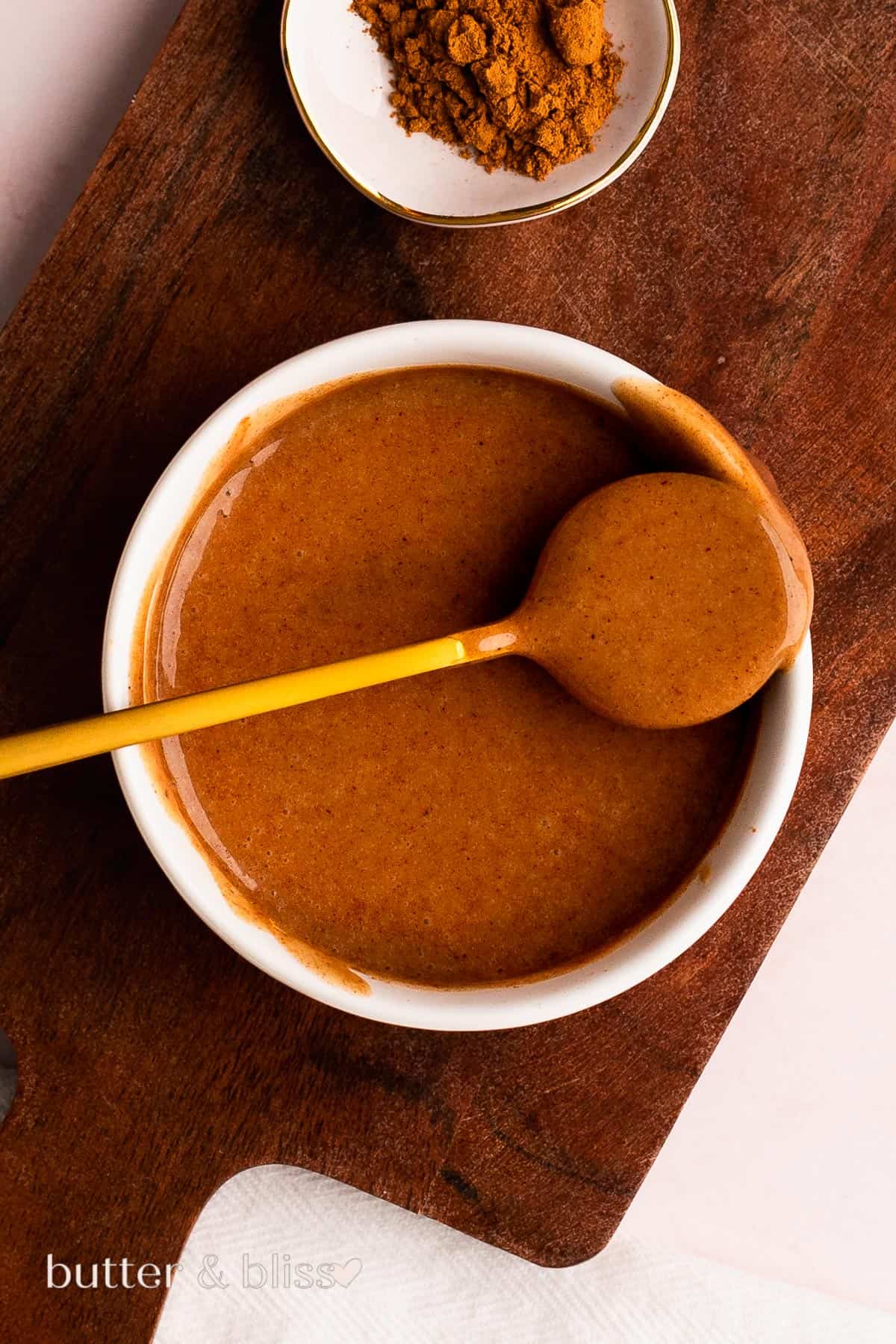 Bowl and spoon full of brown butter glaze on a wood plate.