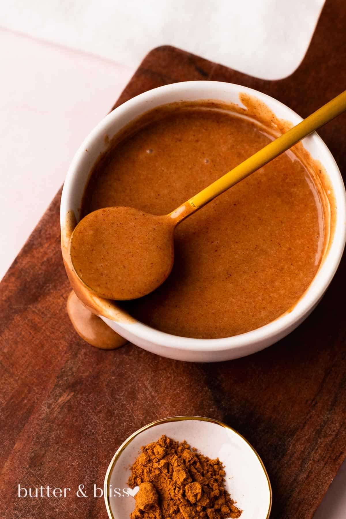 Small bowl full of brown butter cinnamon glaze on a wood plate.