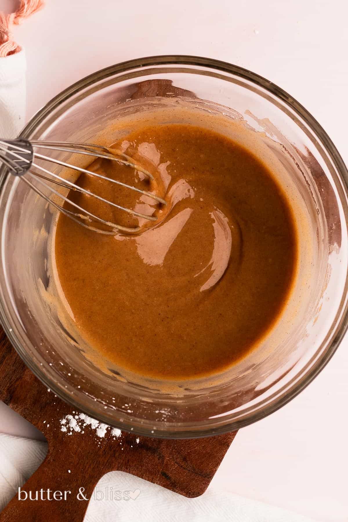 Brown butter glaze being mixed with a whisk in a glass mixing bowl.