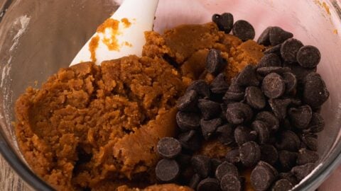 Thick pumpkin cookie bar dough with added chocolate chips in a mixing bowl.