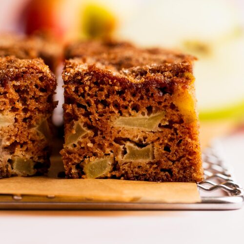 Chunks of apple inside a slice of apple spice cake on a wire cooling rack.