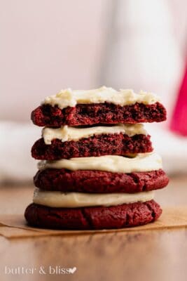 Broken in half red velvet cookie on a stack of more cookies.