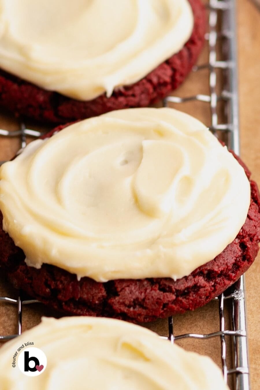 A close of up a cream cheese frosted red velvet cookie on a cooling rack.