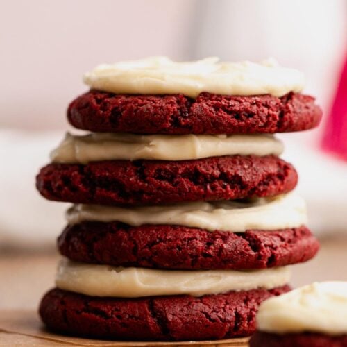 Stack of cream cheese frosted red velvet cookies on a table.