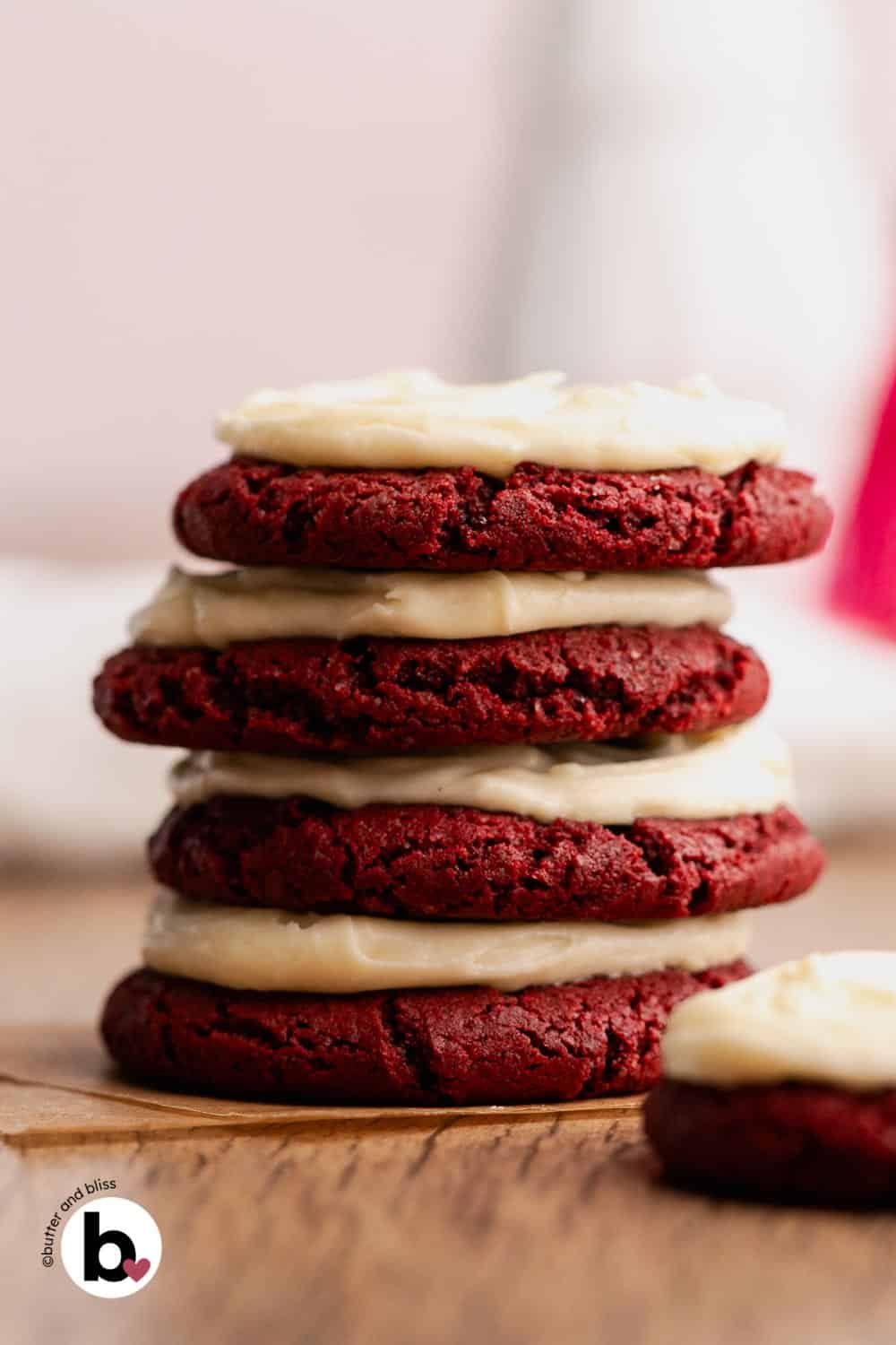 Stack of cream cheese frosted red velvet cookies on a table.