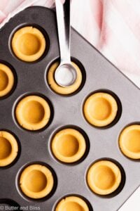 Teaspoon pressing down on cookie dough in a mini muffin tin.