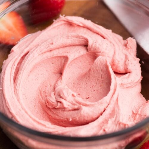A bowl of strawberry frosting on a wood tray.