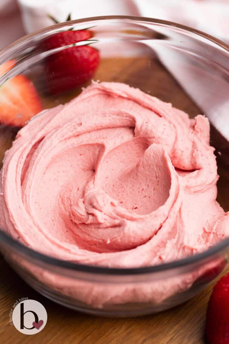 A bowl of strawberry frosting on a wood tray.