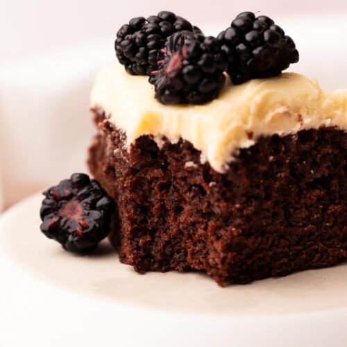 Single slice of moist chocolate cake with vanilla frosting and berries.