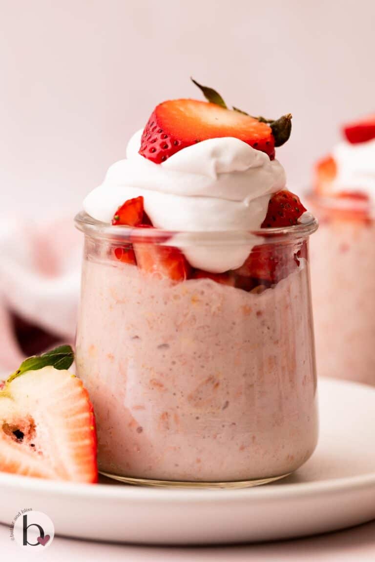 Jar of strawberry oats topped with chopped strawberries and whipped cream.