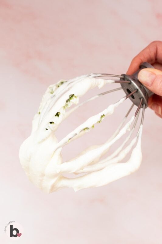 Mixing whisk covered with lime whipped cream.