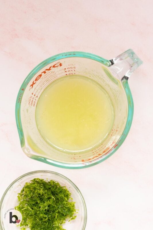 Lime juice in a measuring cup with a bowl of grated lime zest next to it.