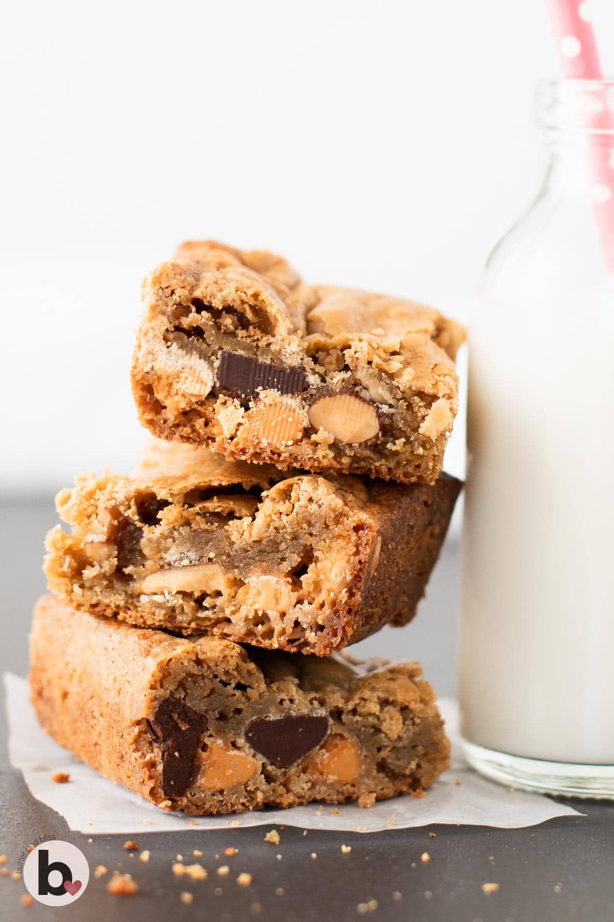 A stack of nut filled blondies leaning against a glass of milk.