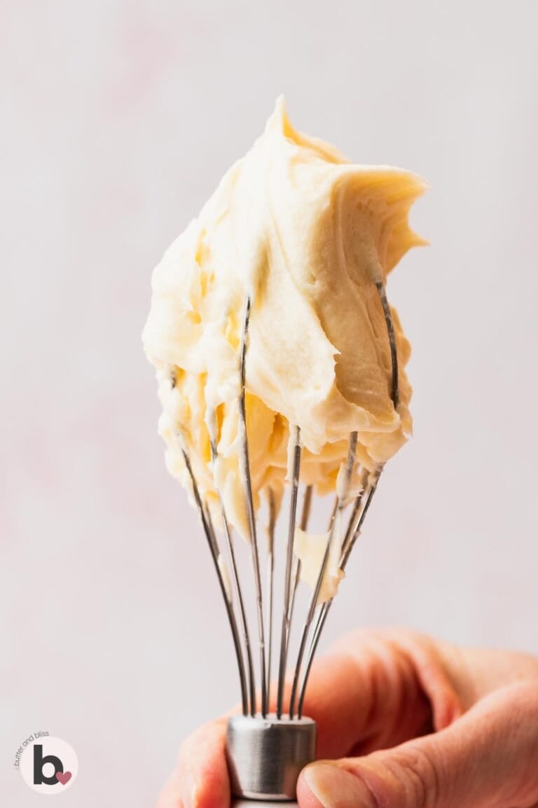 Small batch vanilla frosting on a mixing whisk held by a hand.