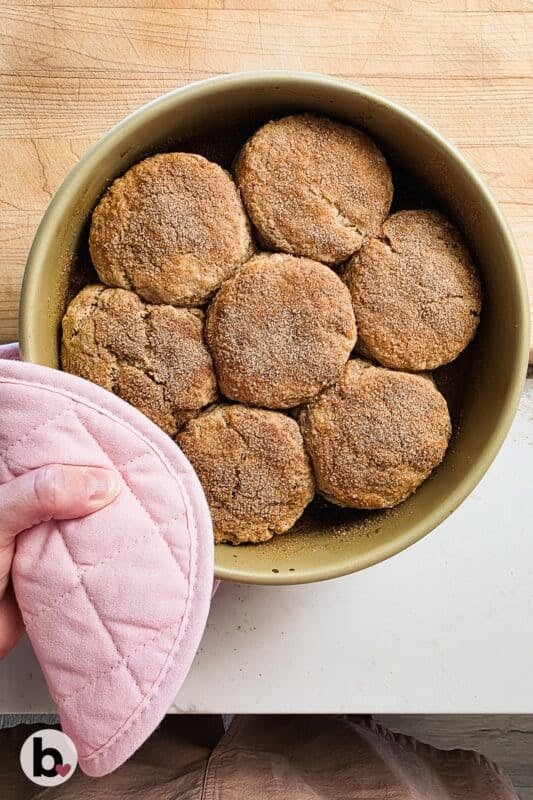 Hand holding a pan of cinnamon biscuits fresh from the oven.