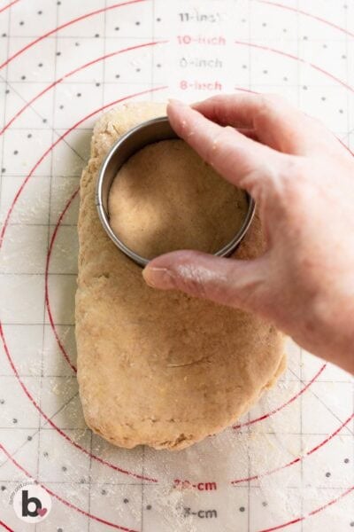 Hand pressing a biscuit cutter down into biscuit dough.