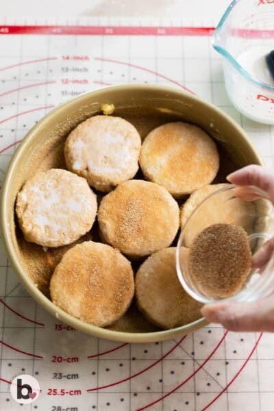 Sprinkling cinnamon sugar over biscuits snuggled into a cake pan.