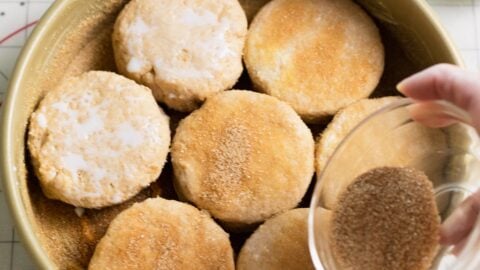 Sprinkling cinnamon sugar over biscuits snuggled into a cake pan.