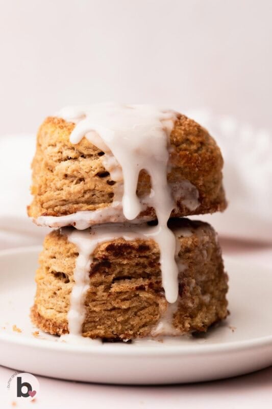 Two cinnamon sugar biscuits drizzled with glaze and stacked on a plate.