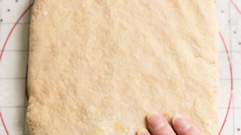Hand flattening dough on a pastry mat.