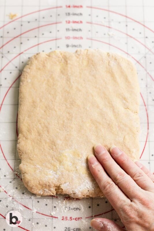 Hand flattening dough on a pastry mat.