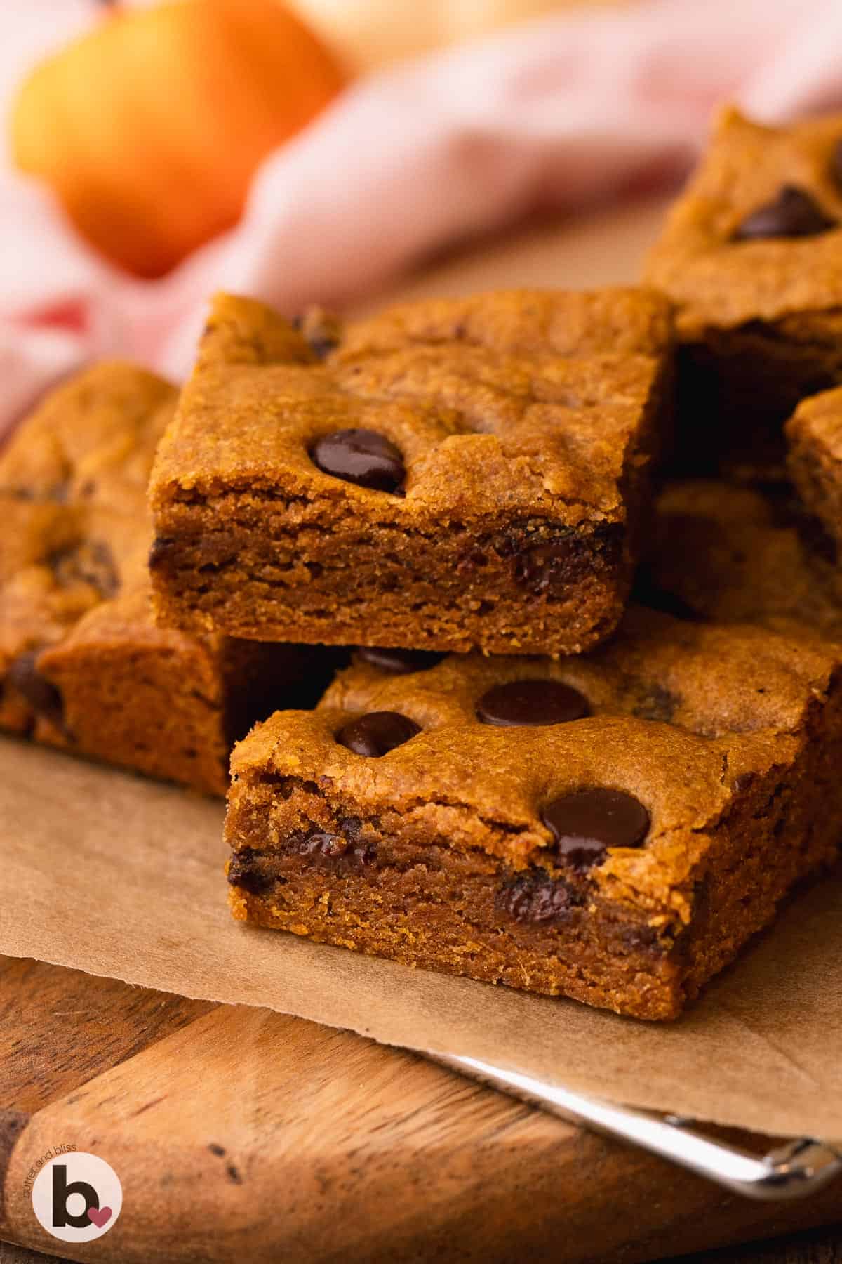 Chewy pumpkin cookie bars with chocolate chips piled on a wood plate.