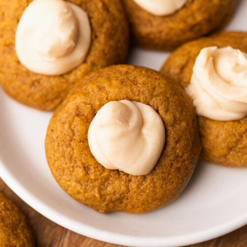 Pumpkin thumbprint cookies with creamy filling on a plate.