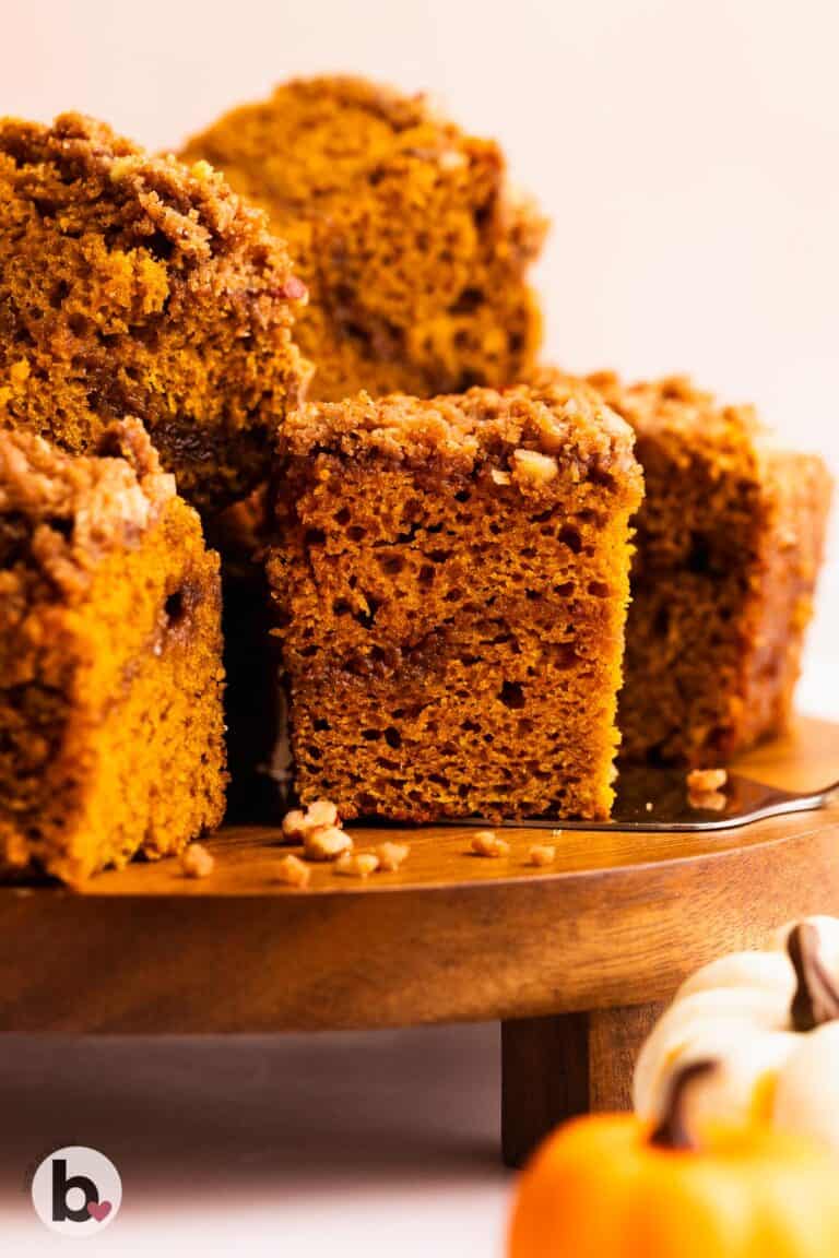Small pumpkin coffee cake cut into squares and stacked on wood platter.