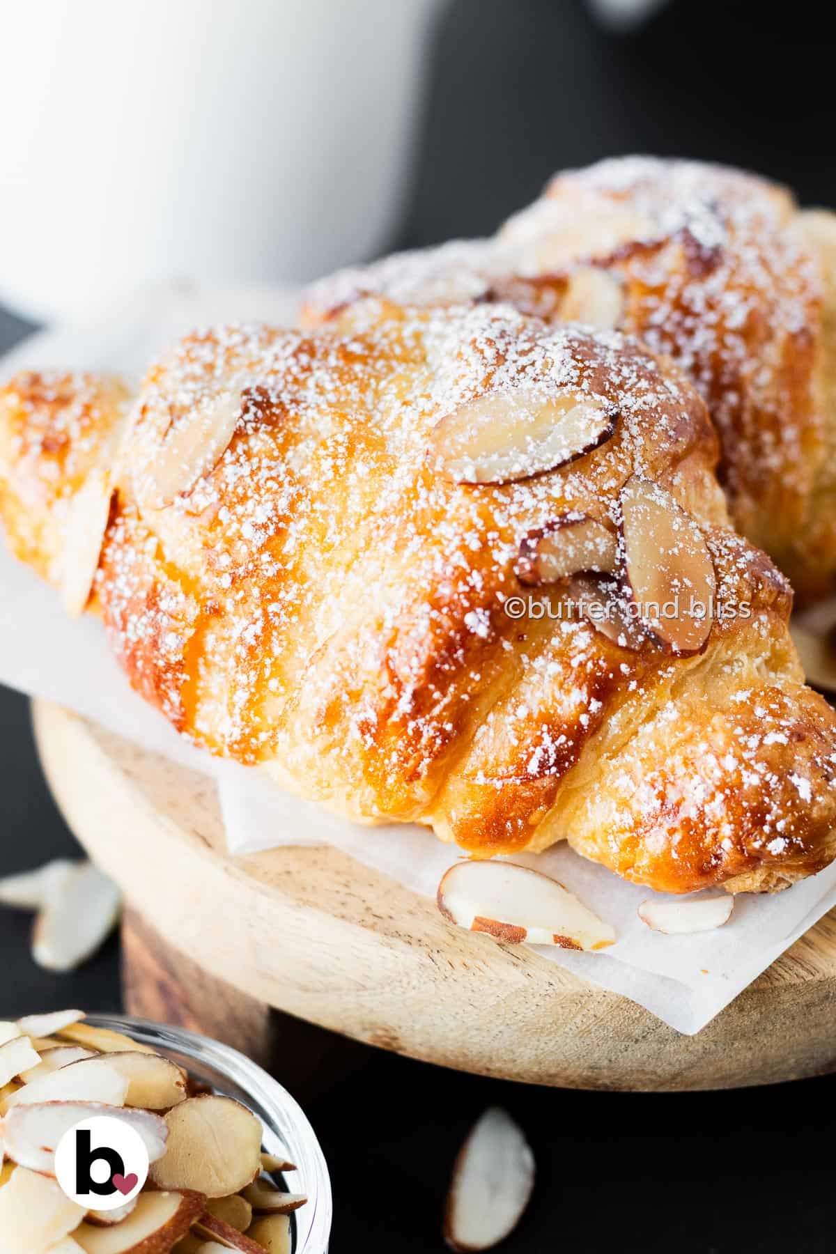 Single homemade almond croissant on a small wood platter.