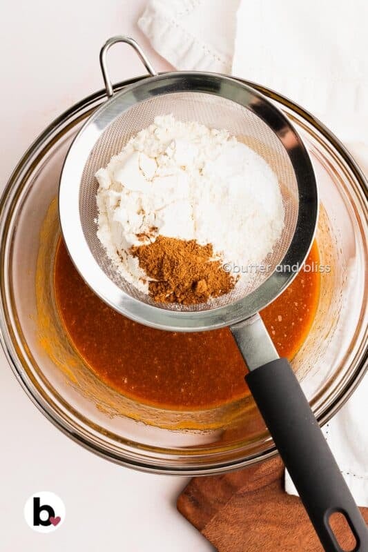 Flour being sifted over wet ingredients in a bowl.