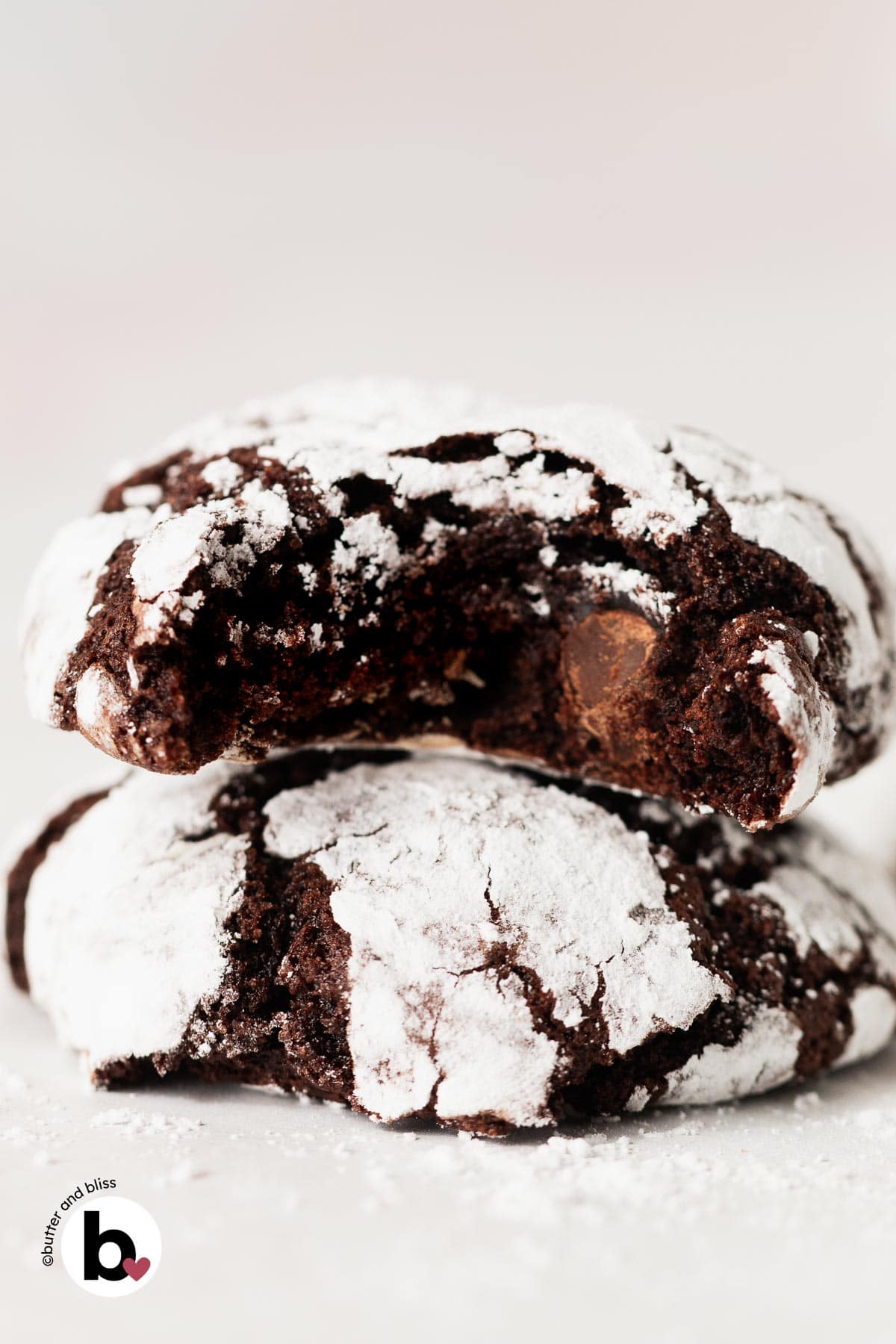 Two fudgy double chocolate crinkle cookies stacked with a bite out of one.