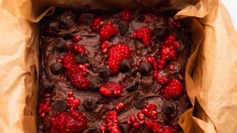 Brownie batter topped with crushed raspberries in a baking pan.