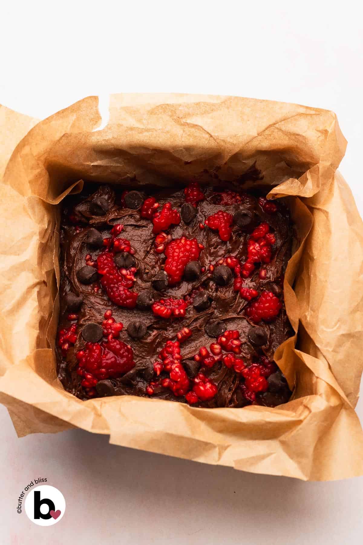 Brownie batter topped with crushed raspberries in a baking pan.